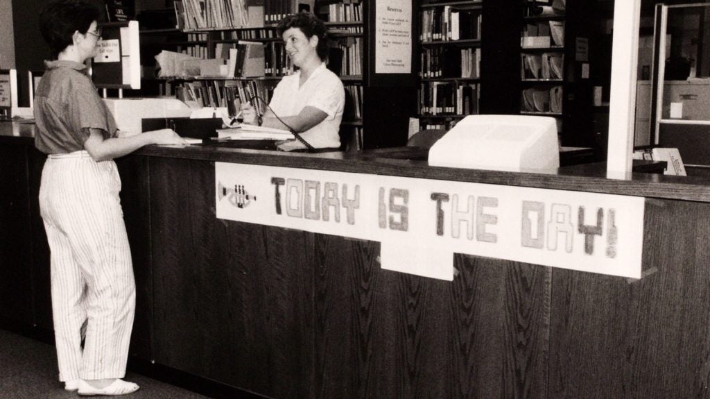 Donna May and Alice Clark (behind desk) in 1985 the day LS/2000 (our Integrated Library System) was introduced