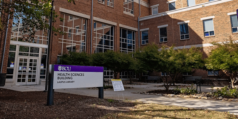 An entrance sign in front of brick library building.