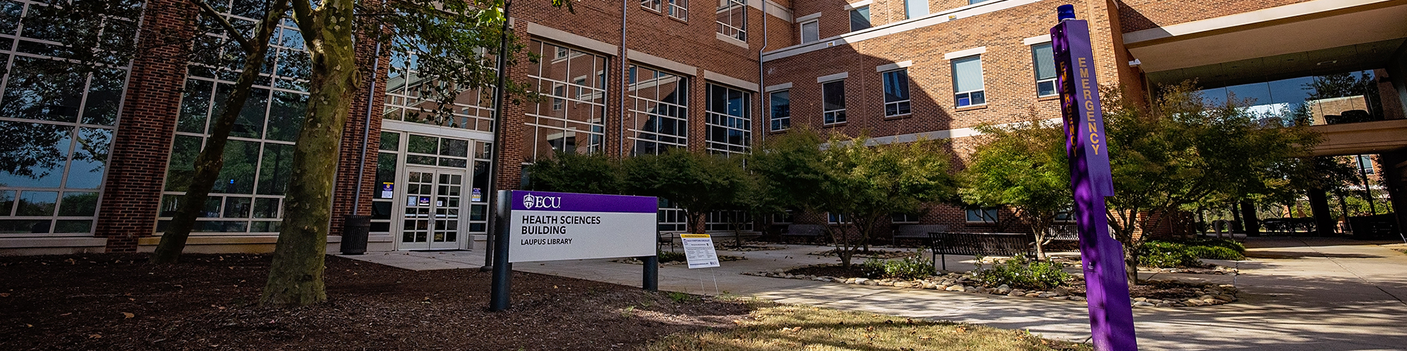 An entrance sign in front of brick library building.